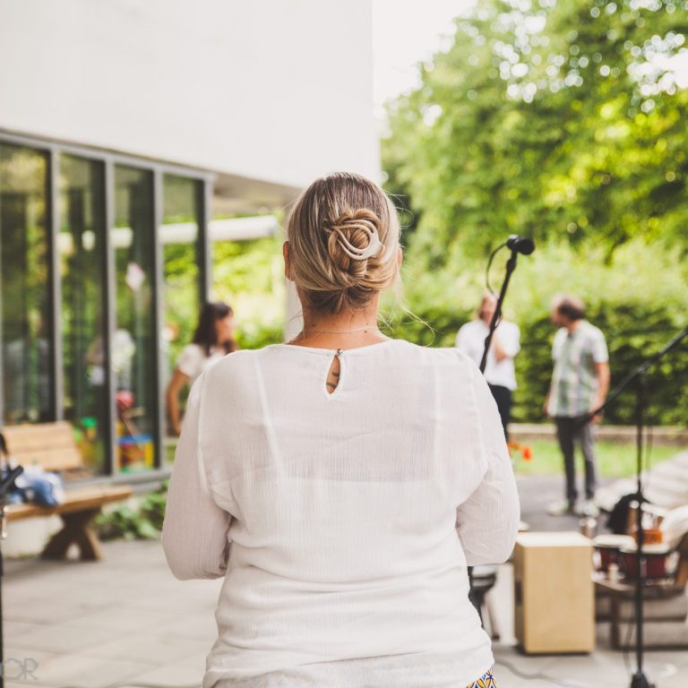 Frau mit Hochsteckfrisur sieht einer Gruppe von Menschen beim Musizieren zu.
