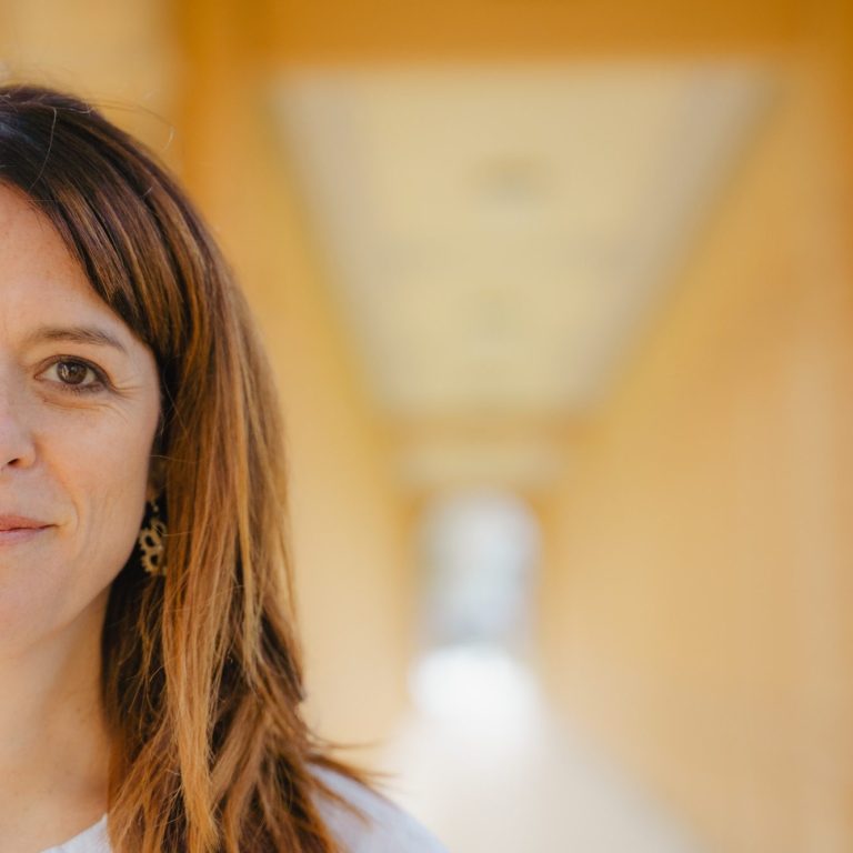 Nahaufnahme einer Frau mit braunen Haaren in einem hellen, orangefarbenen Gang.